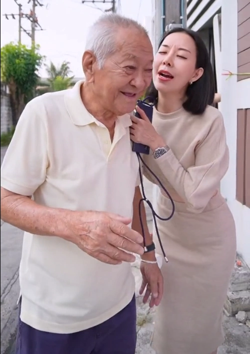 77-year-old Thai grandpa standing next to a large vinyl banner advertising his single daughter.