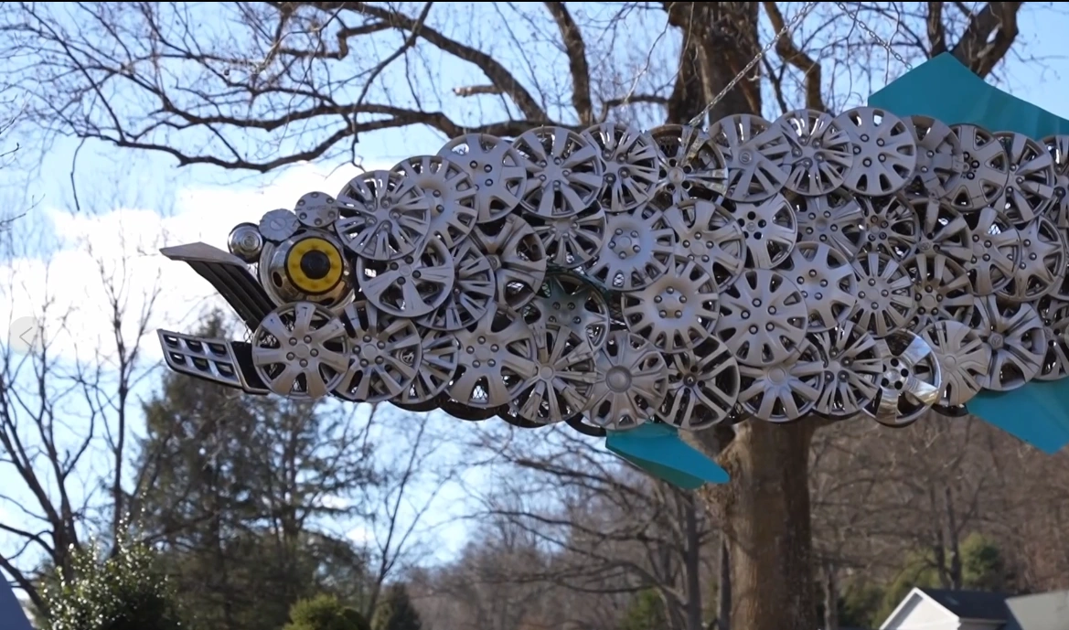 Close-up detail of various silver car hubcaps arranged artistically on a chain-link fence.