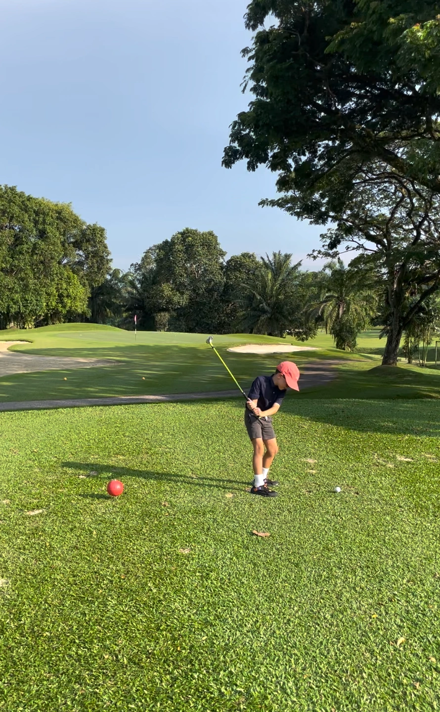 A 6-year-old Singaporean boy named Henry posing confidently with his golf club on a green course.