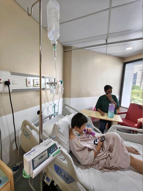 10-year-old Malaysian boy holding father's hand in hospital bed before bone marrow transplant.