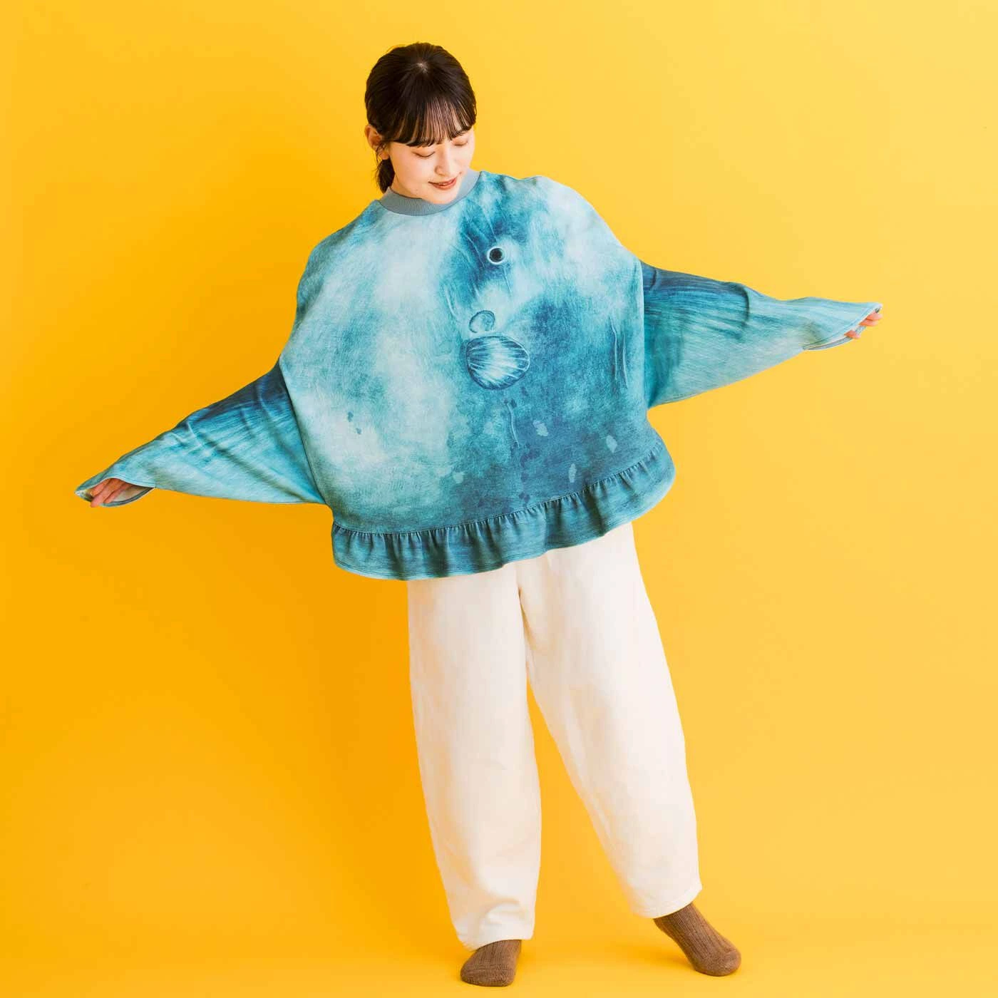 A model wearing the giant, grey knitted Ocean Sunfish (Mola Mola) sweater from Japan, with arms extended into the fins to show its unique shape and face design.