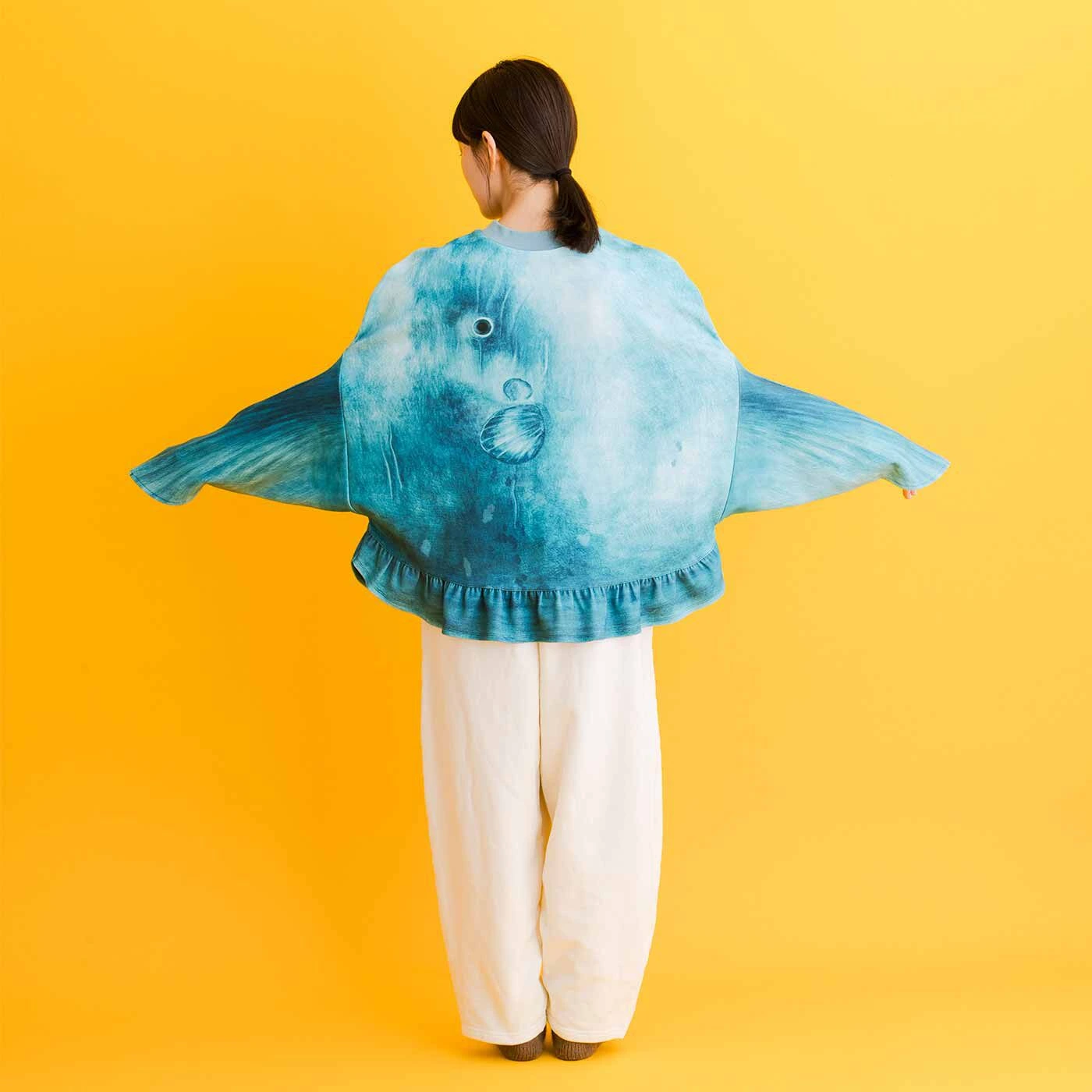 A model wearing the giant, grey knitted Ocean Sunfish (Mola Mola) sweater from Japan, with arms extended into the fins to show its unique shape and face design.