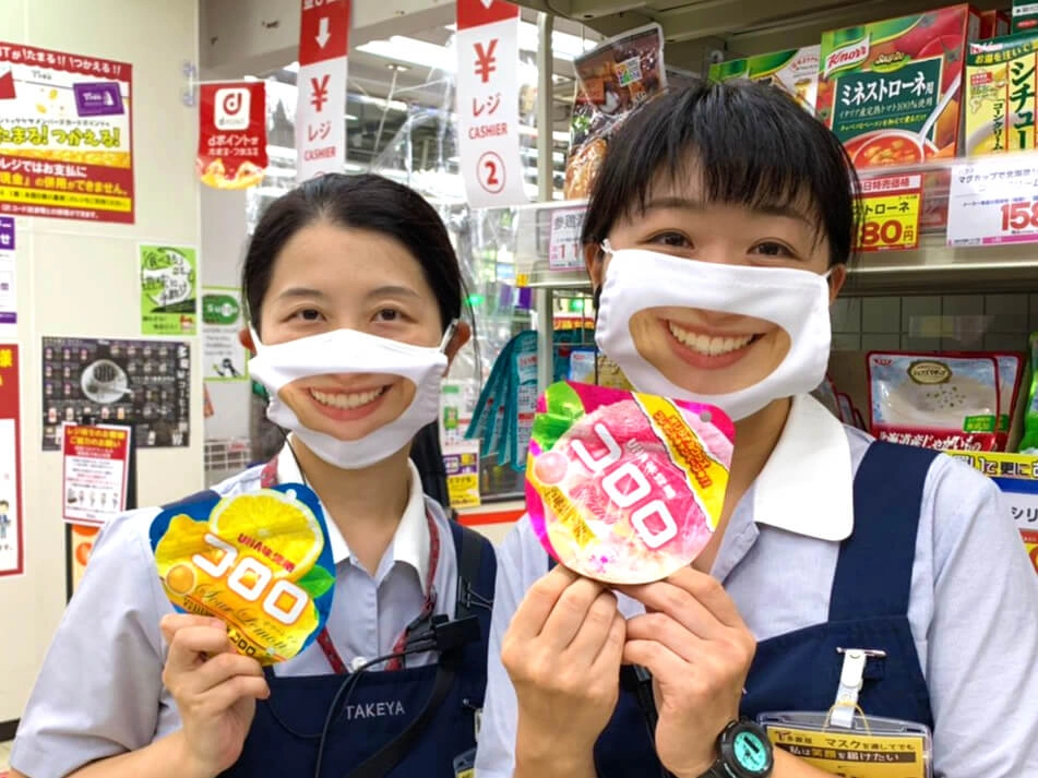 Portrait of a Japanese retail worker wearing the viral realistic smiling face covering as part of a customer service initiative.