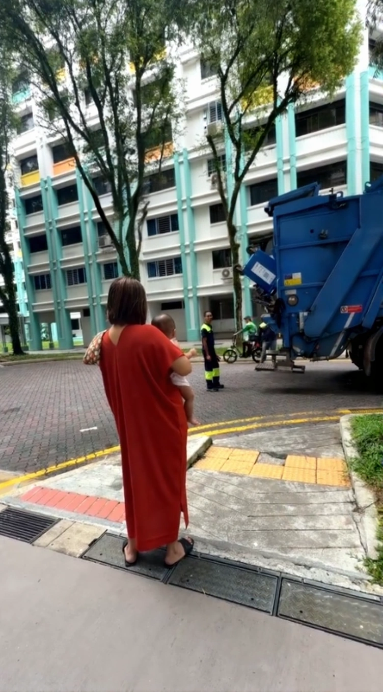  A Singaporean father in high-visibility work uniform waving to his baby daughter from a garbage truck.