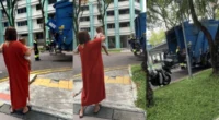 A waste management truck operating in a Singapore residential neighborhood during daylight hours.