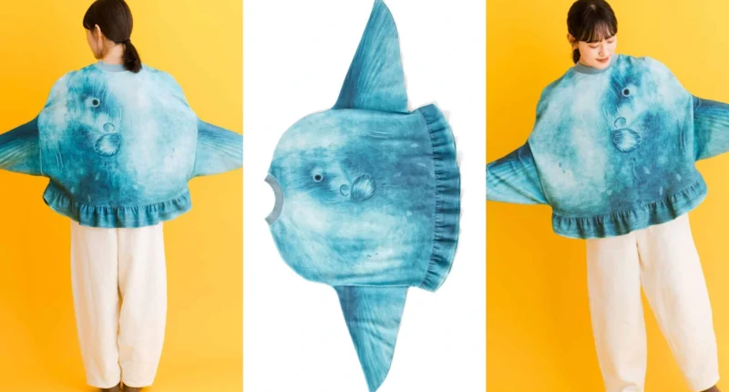 A model wearing the giant, grey knitted Ocean Sunfish (Mola Mola) sweater from Japan, with arms extended into the fins to show its unique shape and face design.