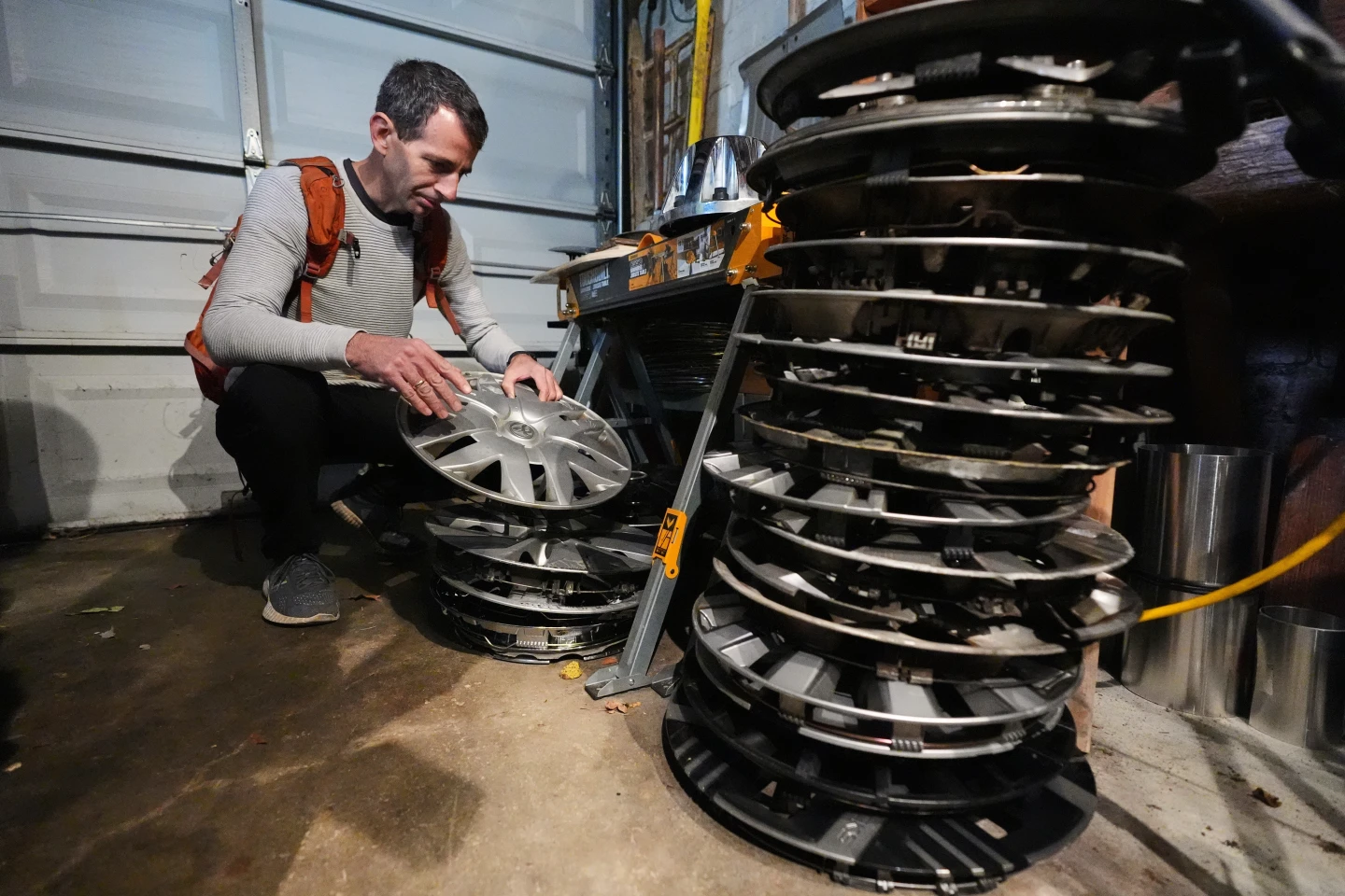 Artist Ken meticulously attaching a salvaged hubcap to a fence using zip-ties.